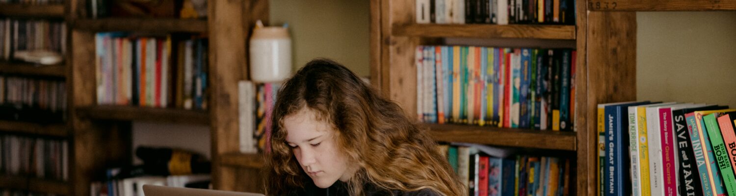 women using a computer in front of a full bookshelf