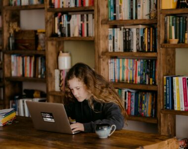 women using a computer in front of a full bookshelf