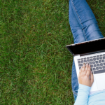 Student sitting on the grass typing on a laptop