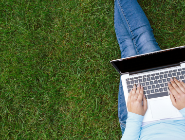 Student sitting on the grass typing on a laptop