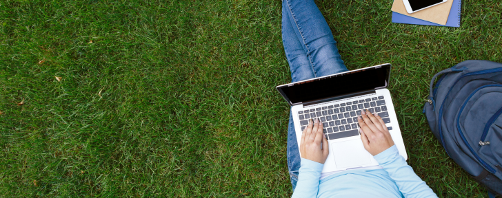 Student sitting on the grass typing on a laptop